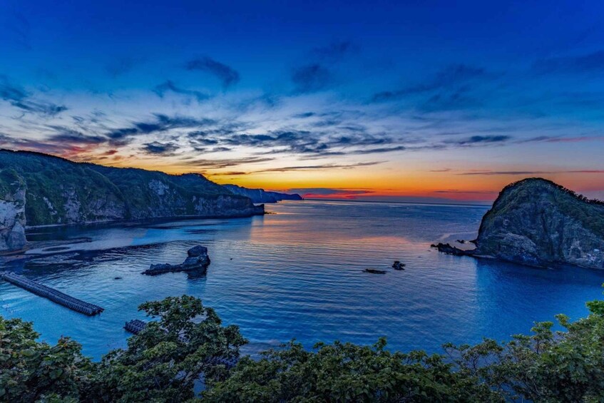 A coastal landscape with a sunset, calm sea, rocky cliffs, and a pier. 2