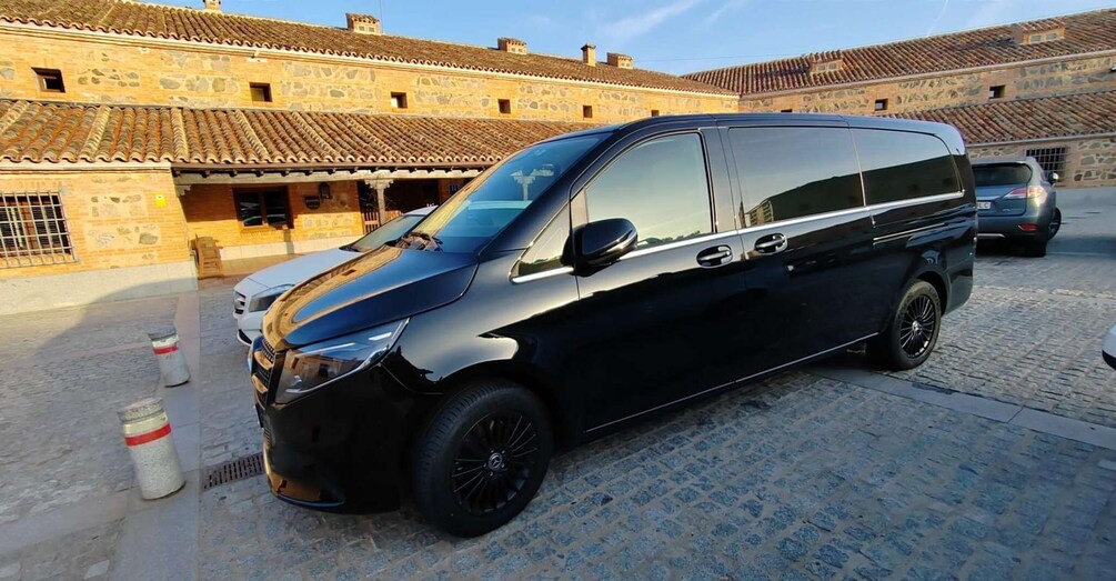 A black van parked on a cobblestone street with historic buildings in the background. 2