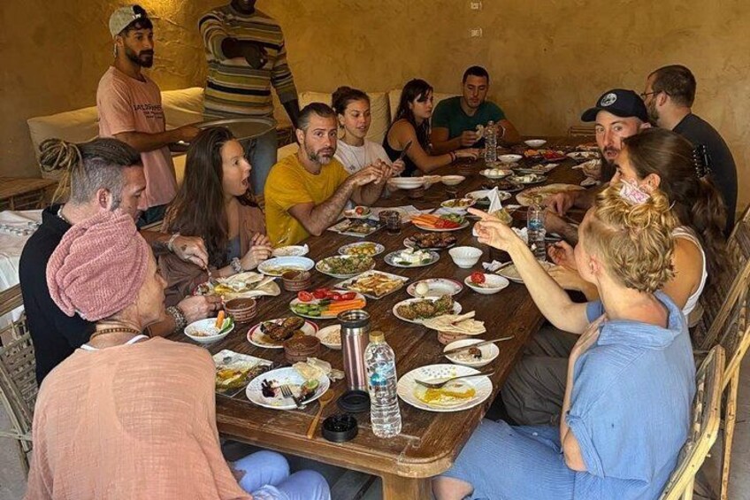 A group of people sitting around a wooden table with various dishes, engaged in a meal. 3