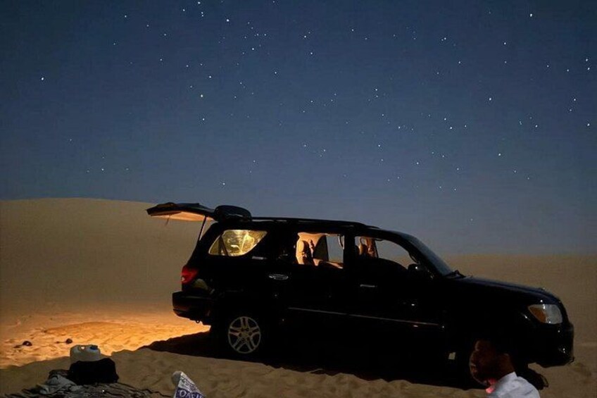 A black SUV parked on a sandy beach under a starry night sky. 4