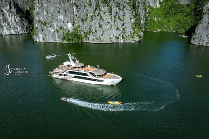 A large yacht named Serenity Grandeur on calm waters with a rocky cliff in the background. 1