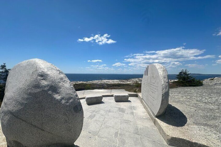 A stone monument with inscriptions, a clear sky, and a distant view of the sea. 5