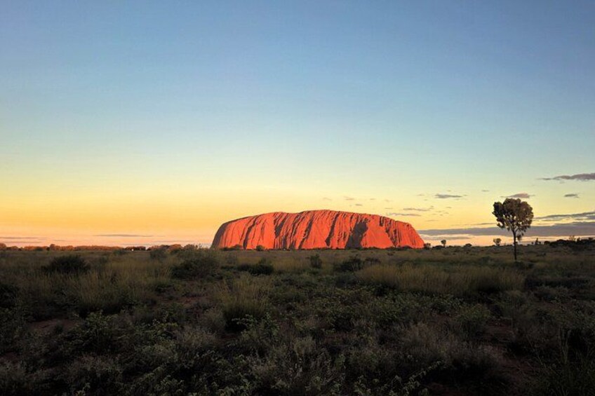 Uluru at sunset with sparse vegetation and a clear sky. 4