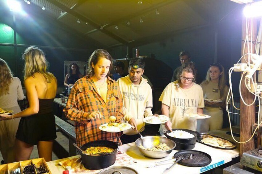 A group of people serving food at a buffet with various dishes and cooking equipment. 2