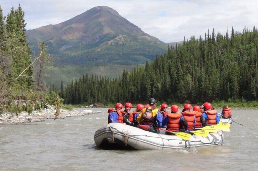 A group of people in a raft on a river with a mountain in the background. 3