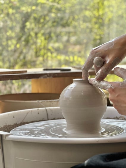 A person shaping a white ceramic pot on a pottery wheel. 1