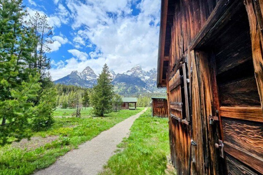 A wooden cabin with a gravel path leading to a mountain backdrop. 3