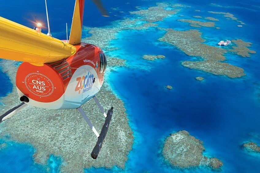 A helicopter with 'CNS AUS' and 'Zoom' logos flying over a coral reef. 1