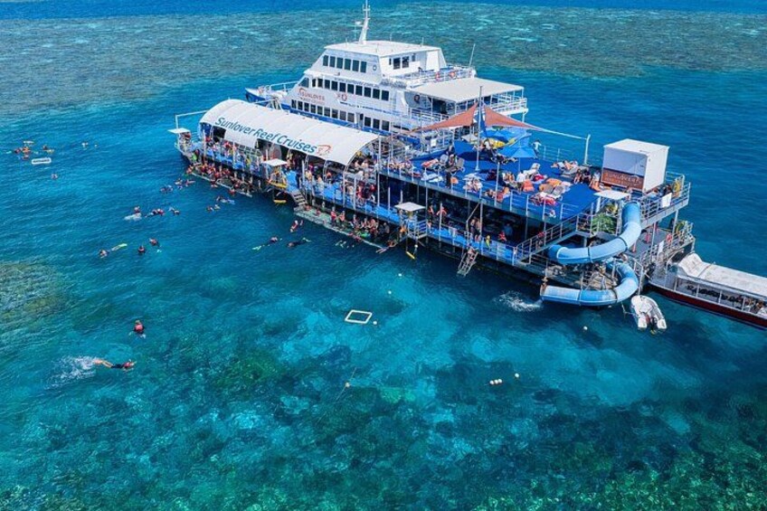 A large cruise ship with people on deck and in the water, surrounded by clear blue ocean. 2