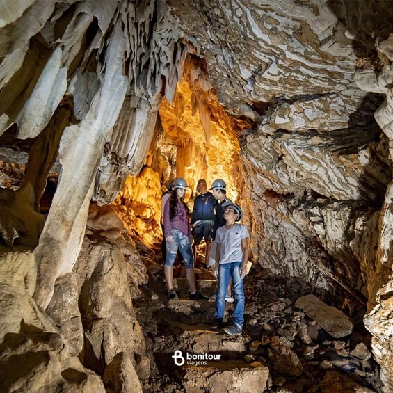 A group of people exploring a cave with stalactites and a warm glow from the cave's interior. 1