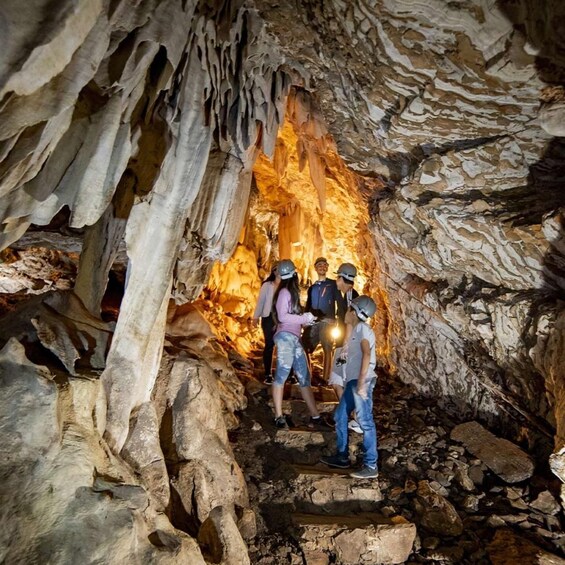 A group of people exploring a cave with stalactites and a warm light source. 4