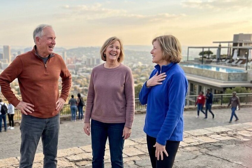 Three people standing on a stone platform with a cityscape in the background. 3