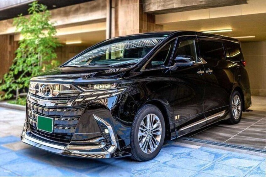 A black Toyota Sienna SUV parked on a tiled surface with a green license plate, surrounded by greenery and a building in the background. 4