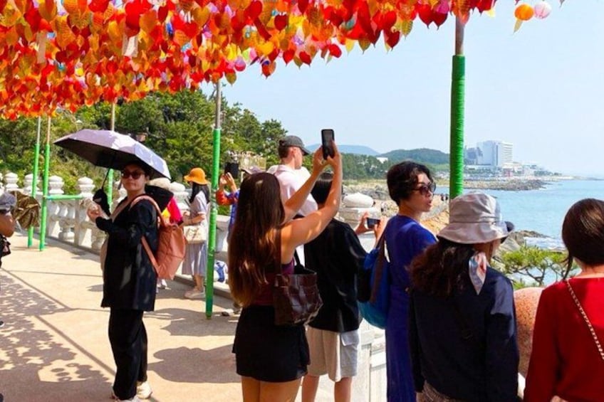 A coastal promenade with people taking photos, a clear sky, and a view of the sea. 2