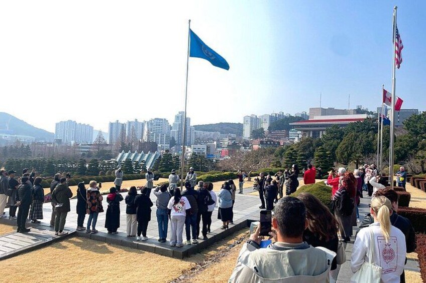 A group of people standing on a platform with flags, overlooking a cityscape with buildings and a hill in the background. 3
