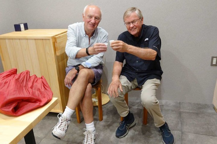 Two men sitting on chairs, one holding a white cup. 5
