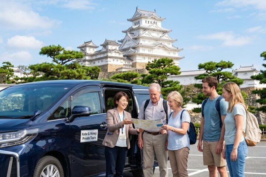 A group of people standing by a dark-colored vehicle with a sign that reads 'Kobe & Himeji Private Tours.' In the background, there is a large white castle-like structure. 1
