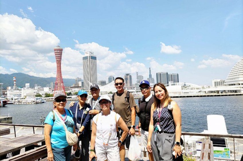 A group of people on a dock with a city skyline and a tower in the background. 1