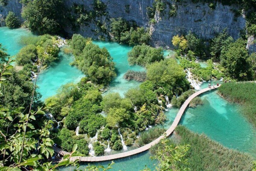 A winding pathway through a lush, tropical landscape with clear turquoise waters and dense greenery. 1