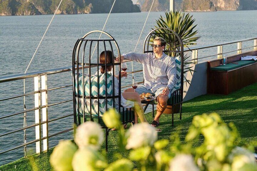 Two people sitting on a deck by a lake, one holding a drink. 2
