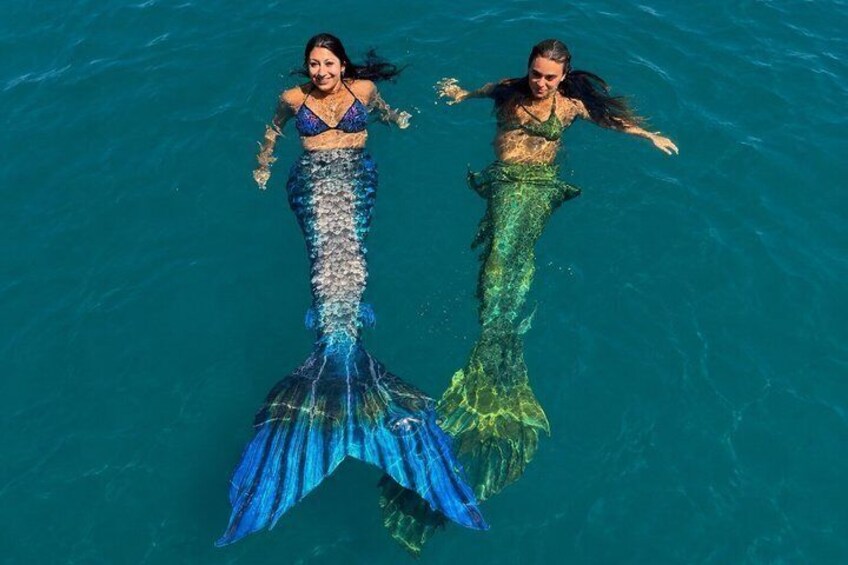 Two mermaids swimming in clear blue water. 1