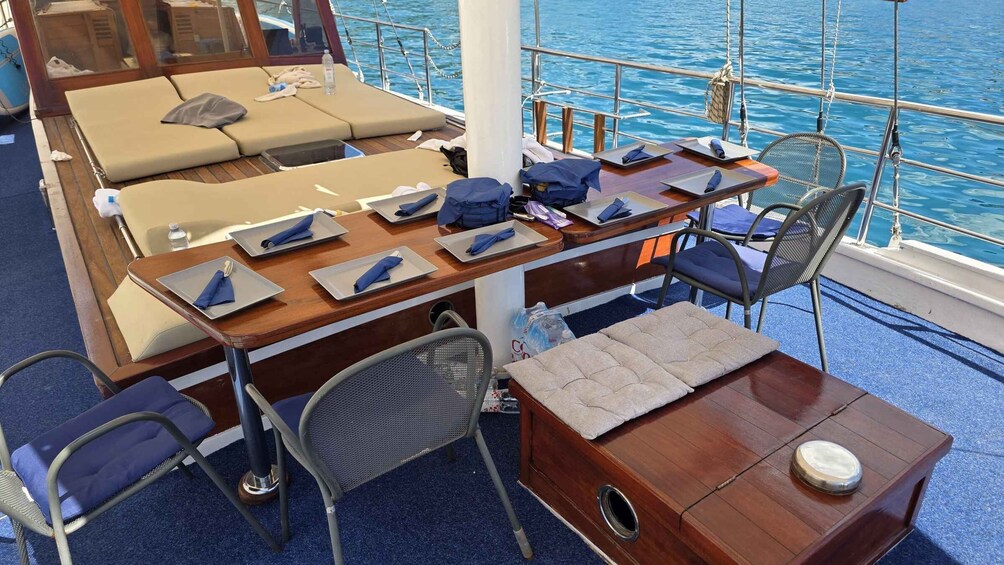 A deck with lounge chairs, a dining table set for four, and a small table with a cushion. 4