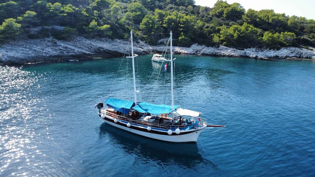 A sailboat anchored in calm waters with a rocky shoreline and dense greenery in the background. 5