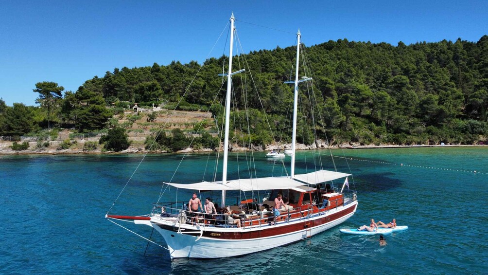 A sailboat with passengers, a smaller boat with people on a float, and a forested coastline. 1
