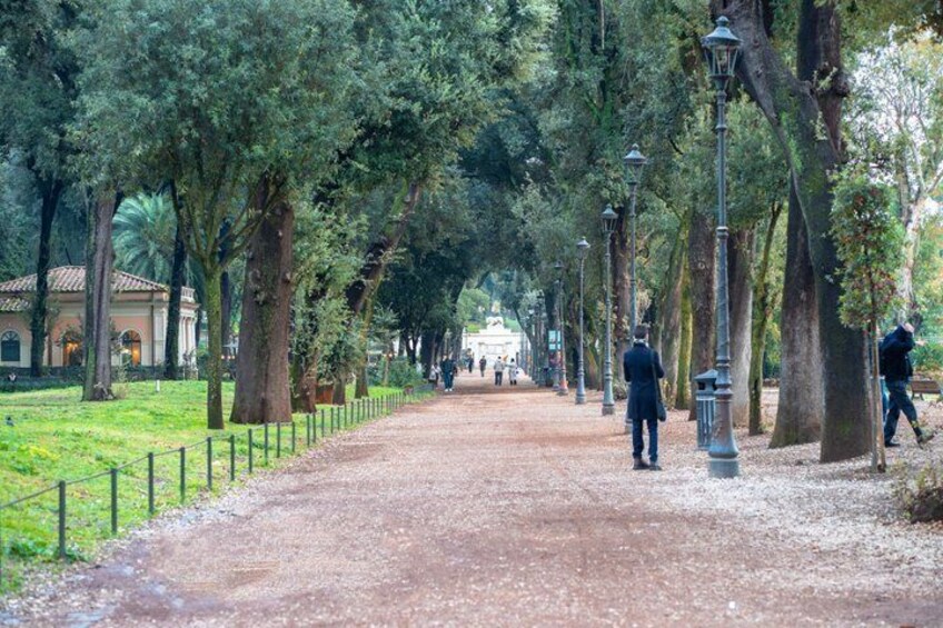 A tree-lined path with lampposts, a fence, and a distant building. 4