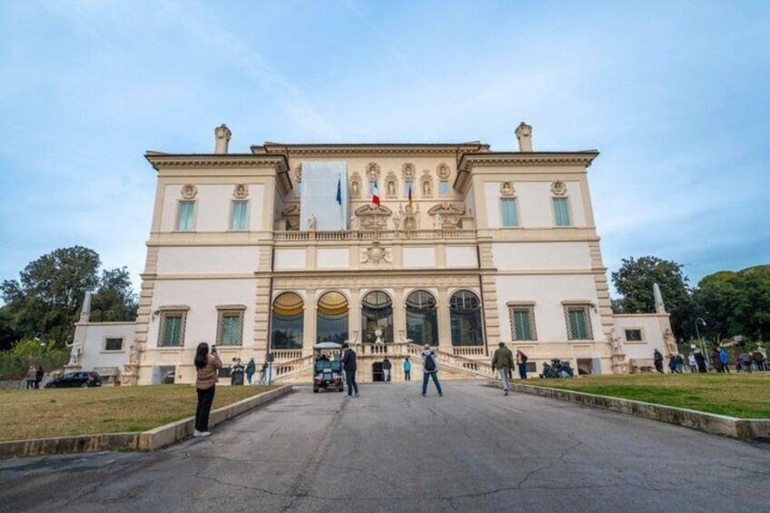 A large, historic building with a central entrance, columns, and a flag. 1