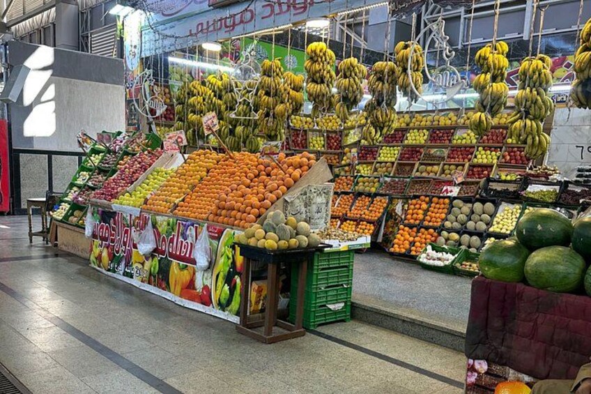 A fruit and vegetable market with various fruits like bananas, oranges, and watermelons on display. 3