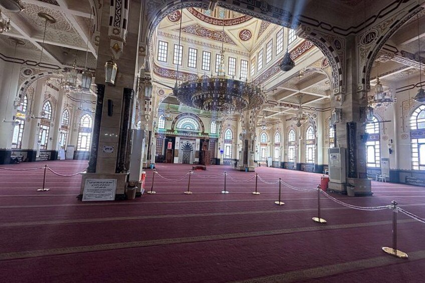 An ornate hall with high ceilings, chandeliers, and a red carpeted floor. 5