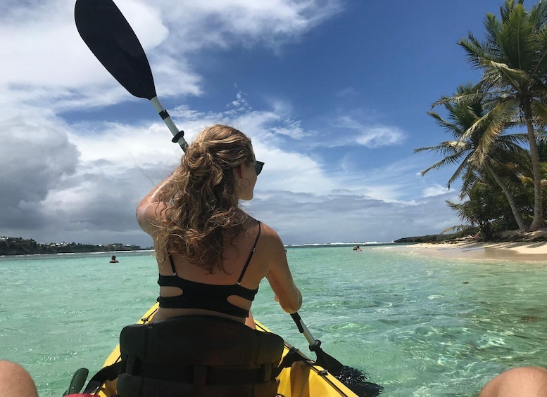 A person kayaking on clear turquoise waters with a beach and palm trees in the background. 1