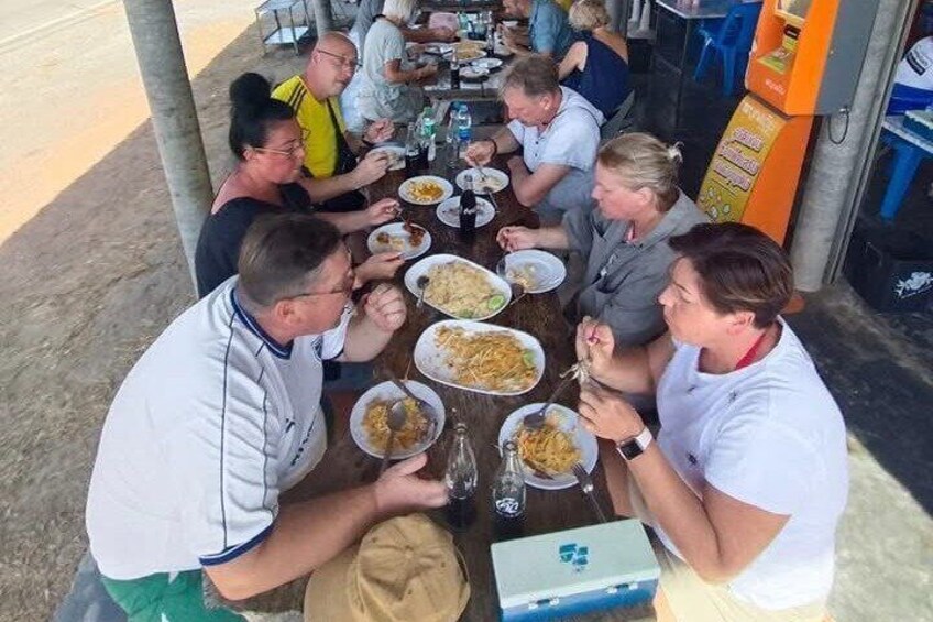A group of people dining at an outdoor table with food and drinks. 3