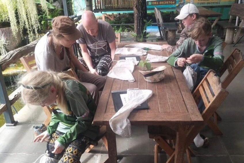 A group of people sitting around a wooden table outdoors, engaged in a discussion or activity. 2