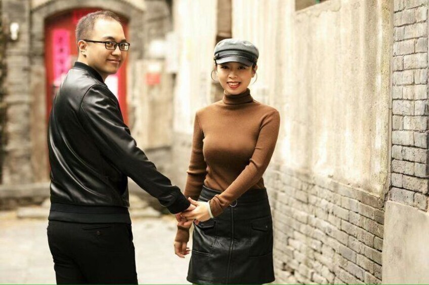 Two people holding hands in an alleyway with brick walls and a red door in the background. 2