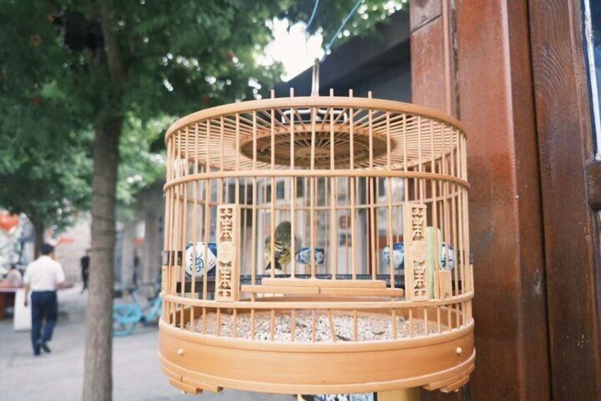 A wooden birdcage with a bird inside, hanging on a wooden post. 5
