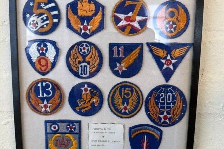 A collection of military badges, each with a unique emblem and number, displayed in a framed arrangement. 5