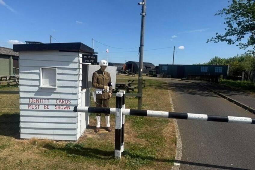 A security checkpoint with a barrier, a sign indicating identity cards must be shown, and a figure in uniform. 4