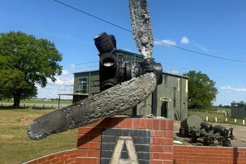 A large, weathered cannon mounted on a brick structure with a grassy field and a building in the background. 3