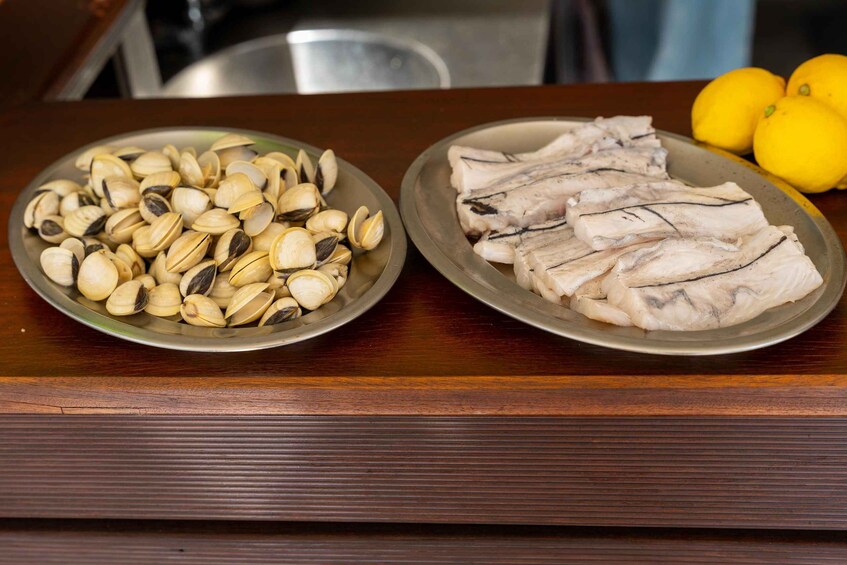 Two plates of seafood, clams and fish, on a wooden table with lemons in the background. 5