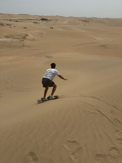 A person riding a board down a sandy dune. 5