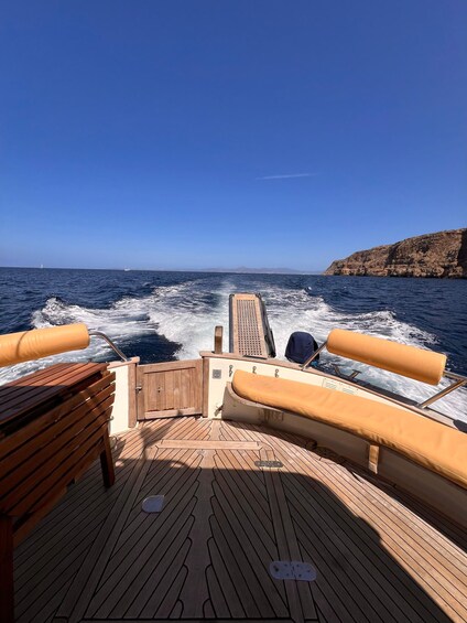 A boat deck with wooden flooring, cushioned seating, and a view of the ocean and distant land. 5