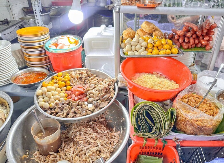 A variety of food items displayed in metal containers and bowls, including noodles, fried snacks, and other street food. 3