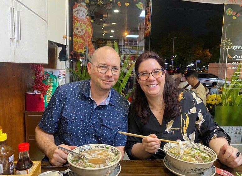 Two people dining at a restaurant with bowls of soup and chopsticks. 1