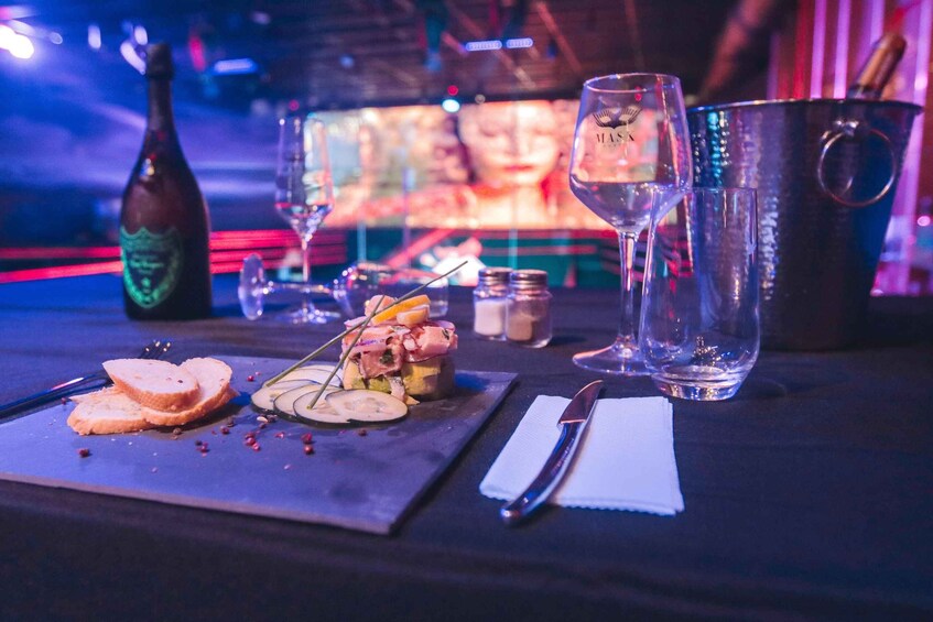A dining table with a bottle, glasses, a knife, a napkin, and a plate with food. 5