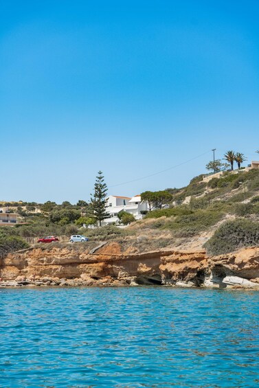 A coastal landscape with clear blue water, rocky cliffs, and houses on a hillside. 3