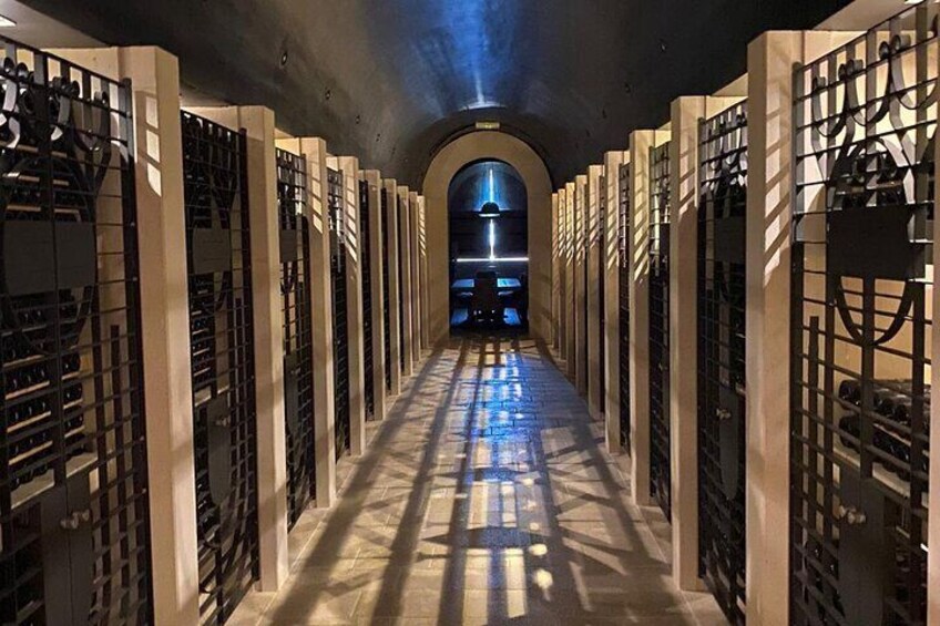 A long, narrow corridor with rows of wine racks on either side, leading to a brightly lit archway at the end. 5