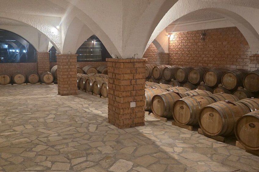 A wine cellar with stone floors and brick walls, featuring rows of wooden wine barrels. 5