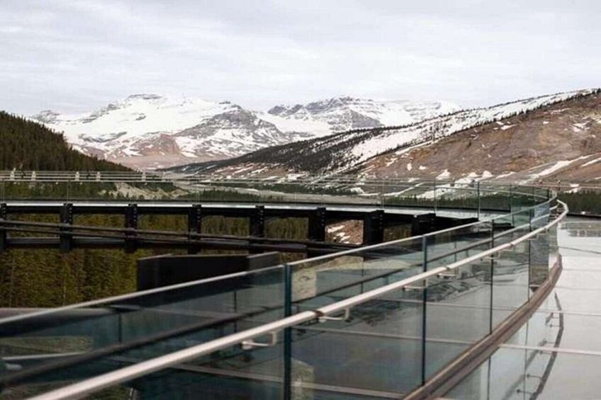 A glass bridge with a metal railing, overlooking a mountainous landscape with snow-capped peaks. 3